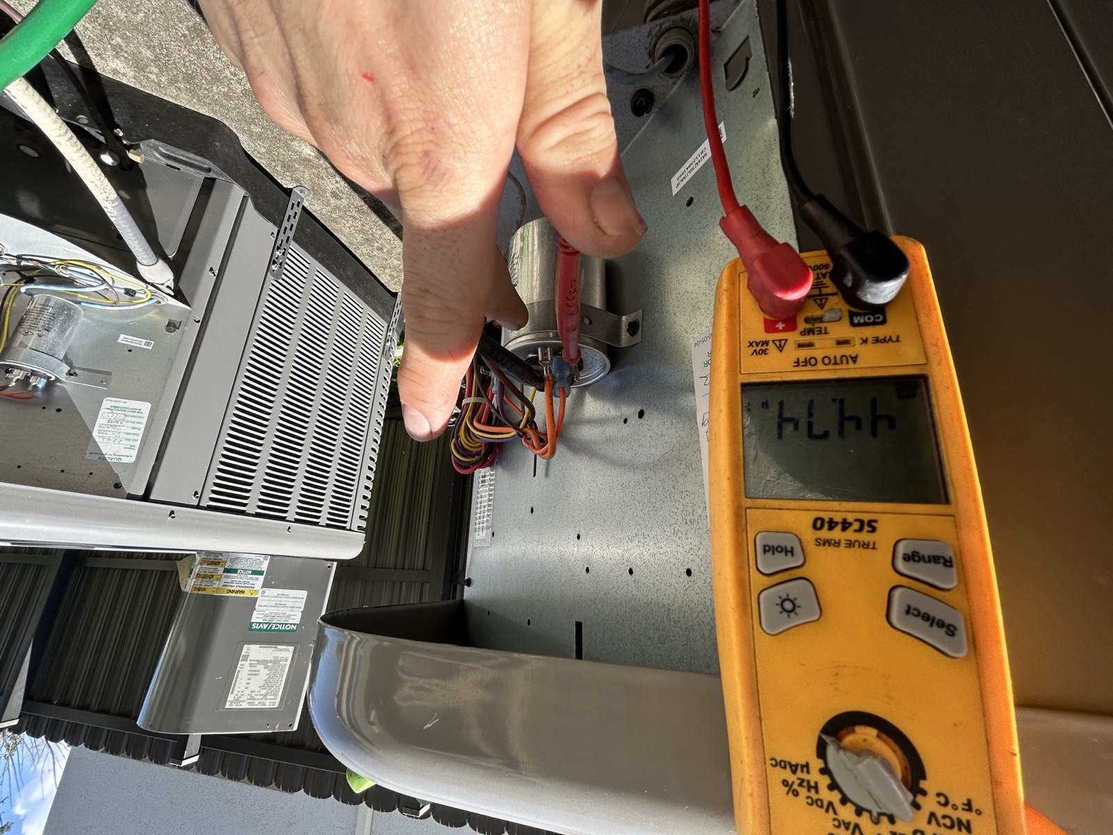 Technician checking an outdoor unit capacitor during an air conditioning service visit